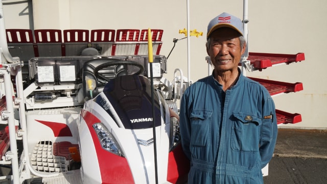 自慢の密苗田植機の前で笑顔を見せる杉本さん。